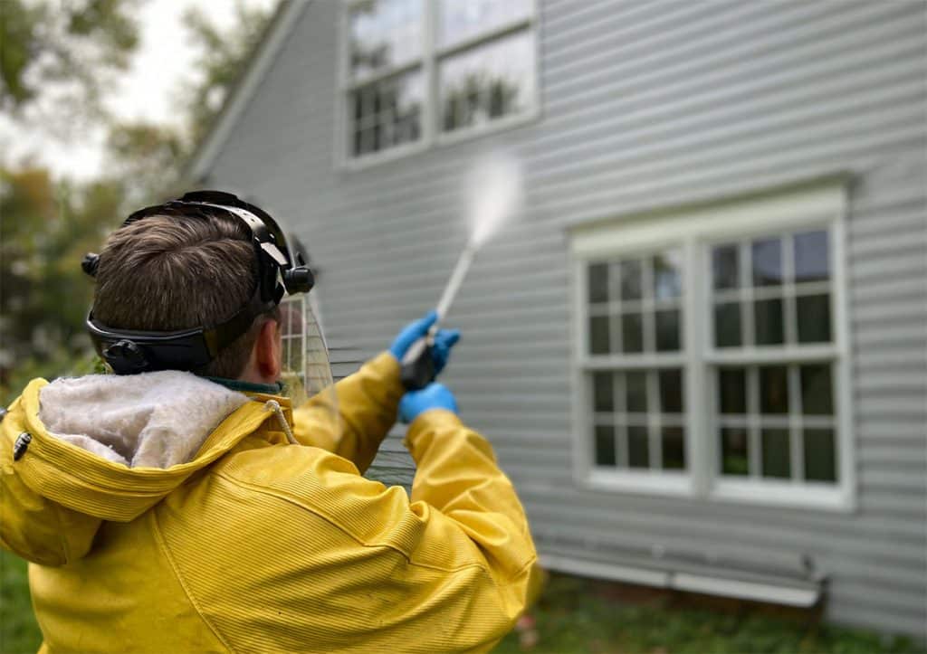 Person pressure washing house siding outdoors